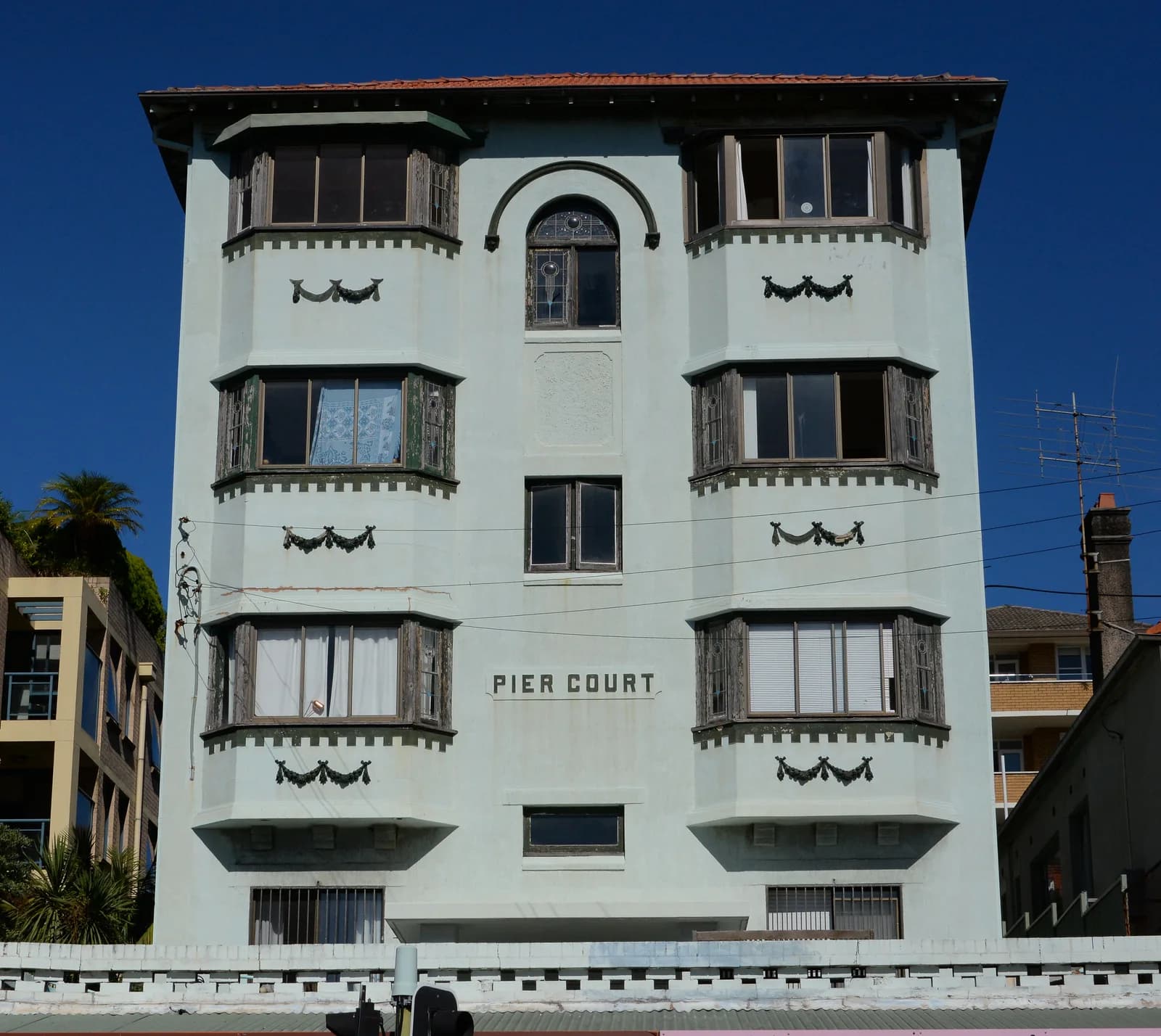 The sunlit facade and bay windows of Pier Court apartments in Coogee, beneath a clear blue sky